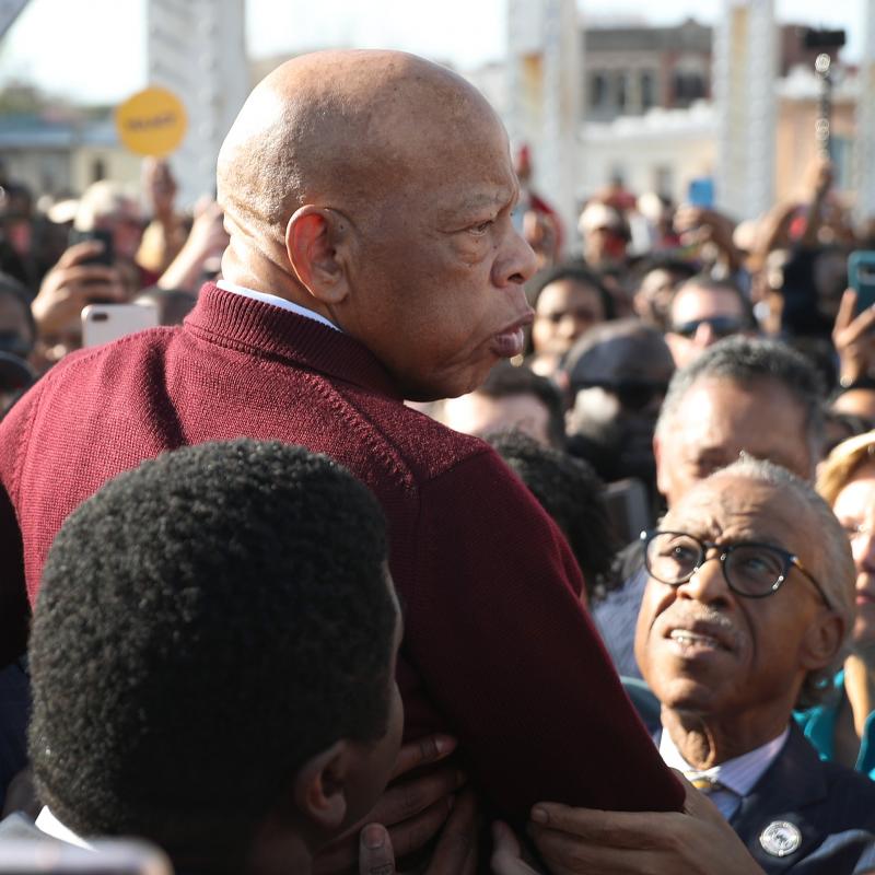 John Lewis being lifted up by a crowd that includes Al Sharpton on the Edmund Pettus bridge on the 55th anniversary of Bloody Sunday