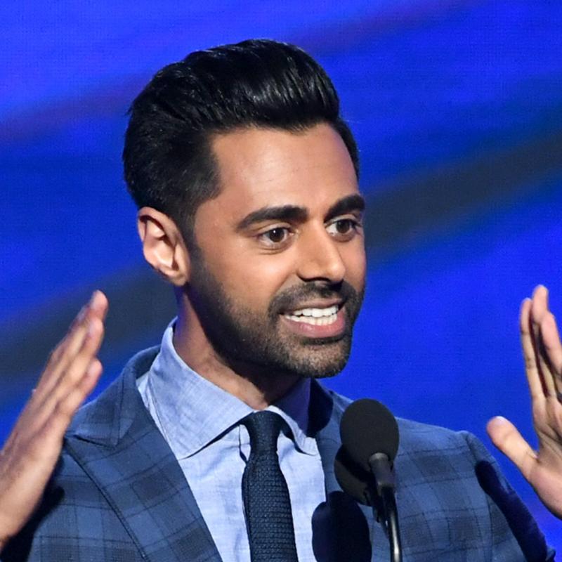 Comedian Hasan Minhaj gestures in front of a microphone