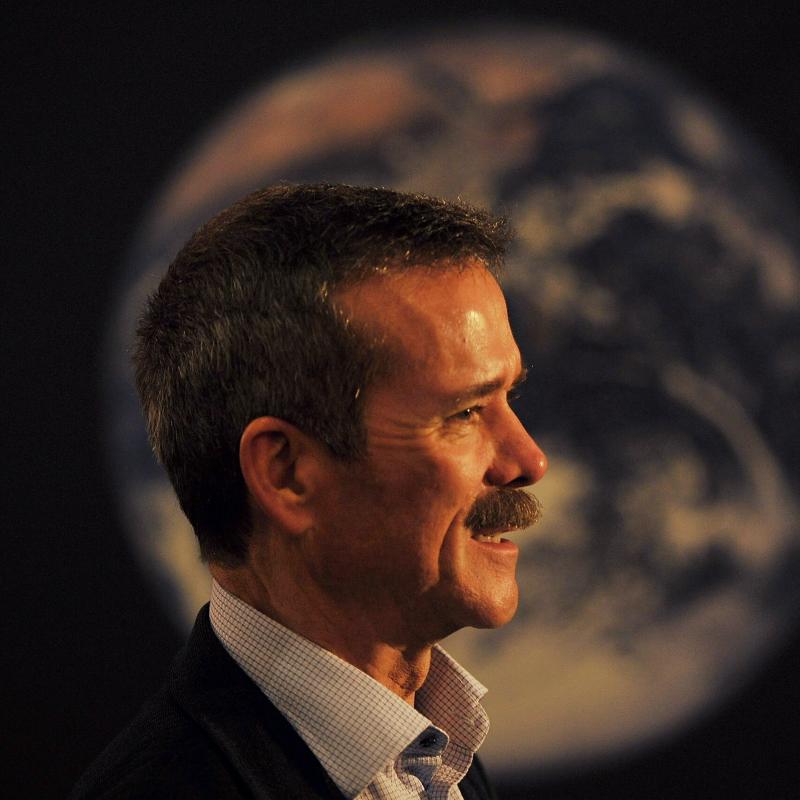 Astronaut Chris Hadfield speaks in front of an image of the Earth taken from outer space.