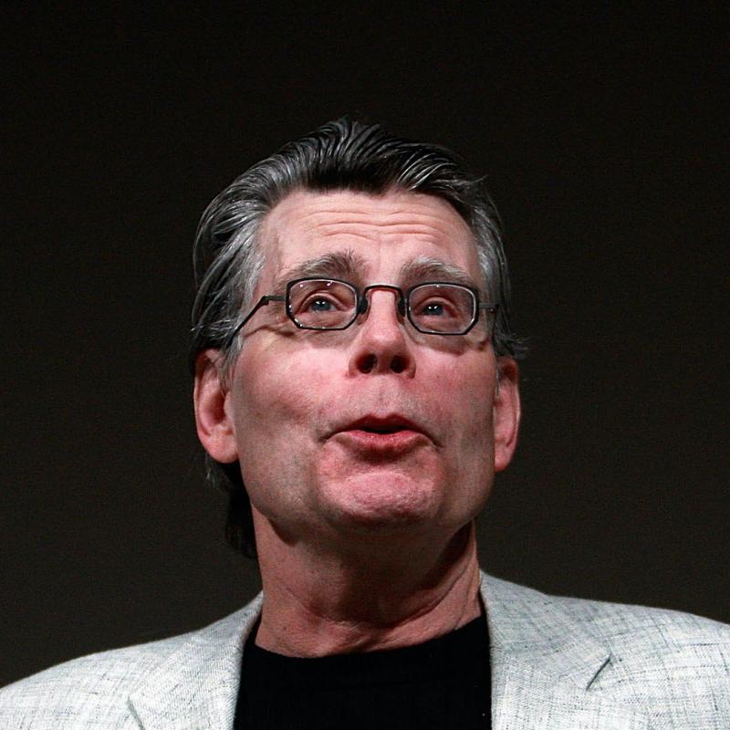 Writer Stephen King looks bemused while speaking against a black background