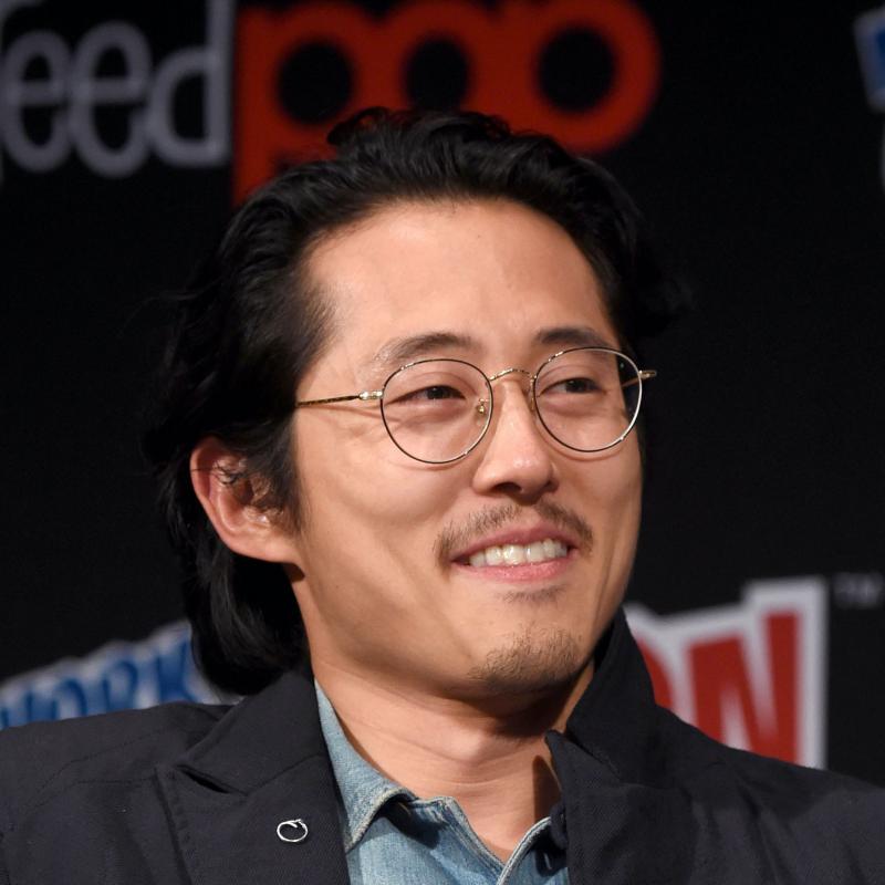 Actor Steve Yeun smiles on stage in a pair of glasses