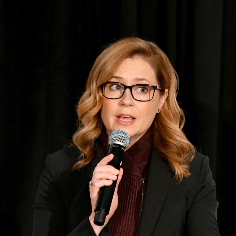 Actress Jenna Fischer speaks into a microphone on stage during a speaking engagement