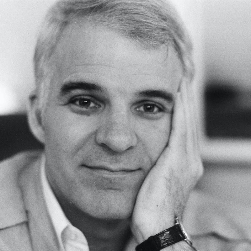 Actor and Comedian Steve Martin looks into the camera with his head resting on his hand in this black and white image from around 1980