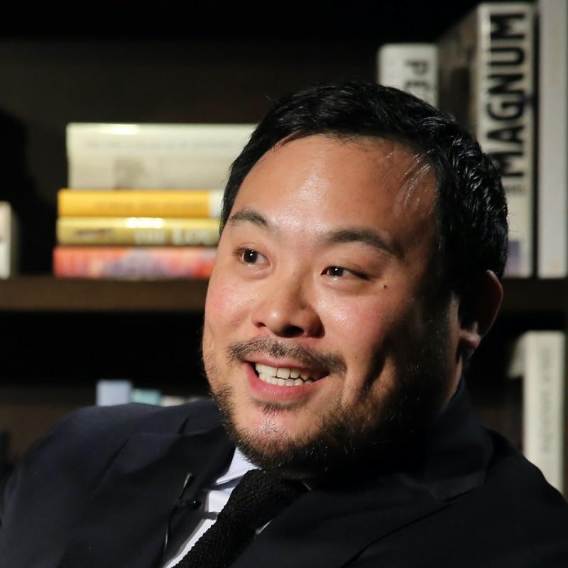 Celebrity chef David Chang smiles in front of a bookshelf