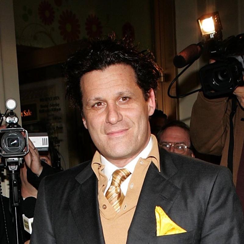 Fashion designer Isaac Mizrahi poses wearing a tan tie and a yellow pocket square
