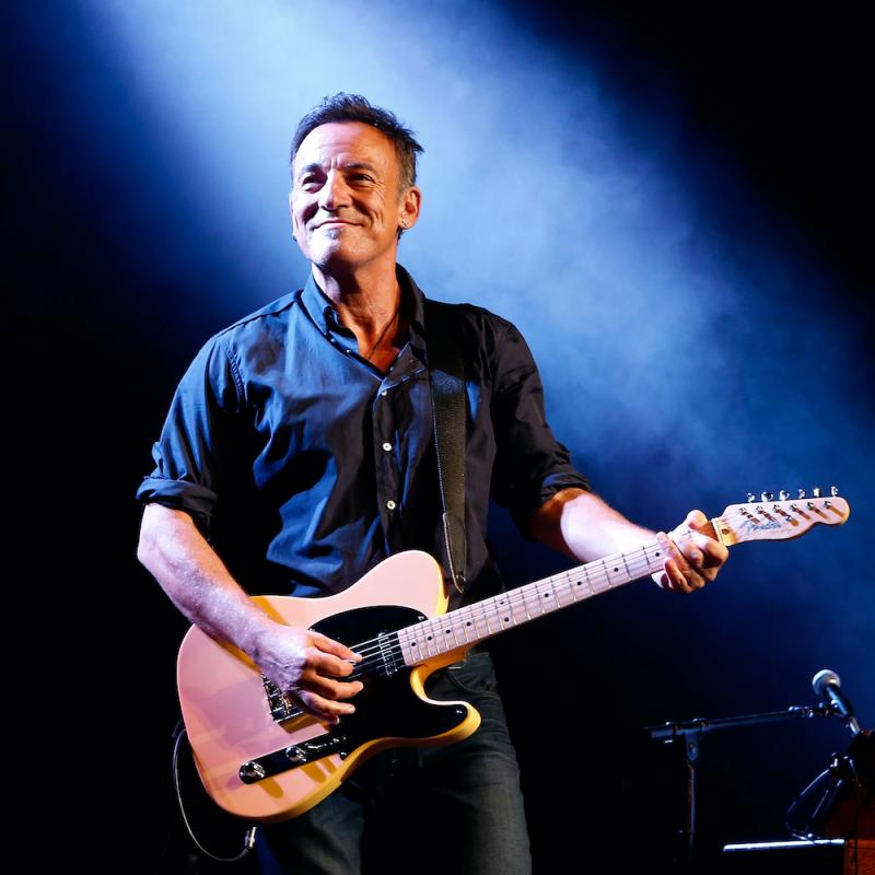 Musician Bruce Springsteen stands on stage with his guitar