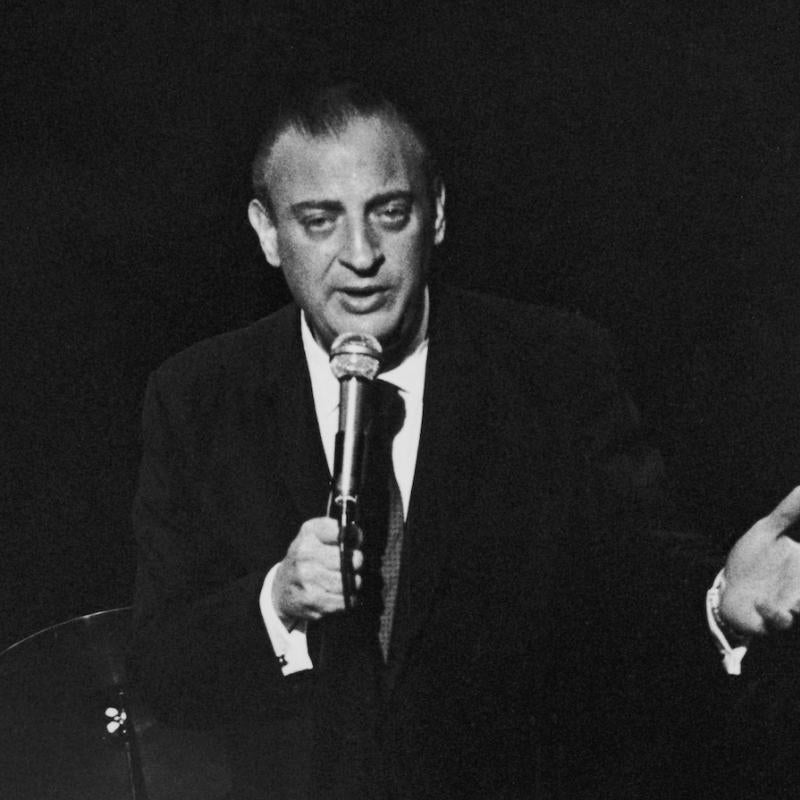Comedian Rodney Dangerfield performs on stage with a mic in his hand